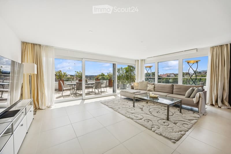Modern living room with large windows and a balcony view, featuring a beige sofa, glass coffee table, floor lamp, TV stand, and dining area with chairs and table.