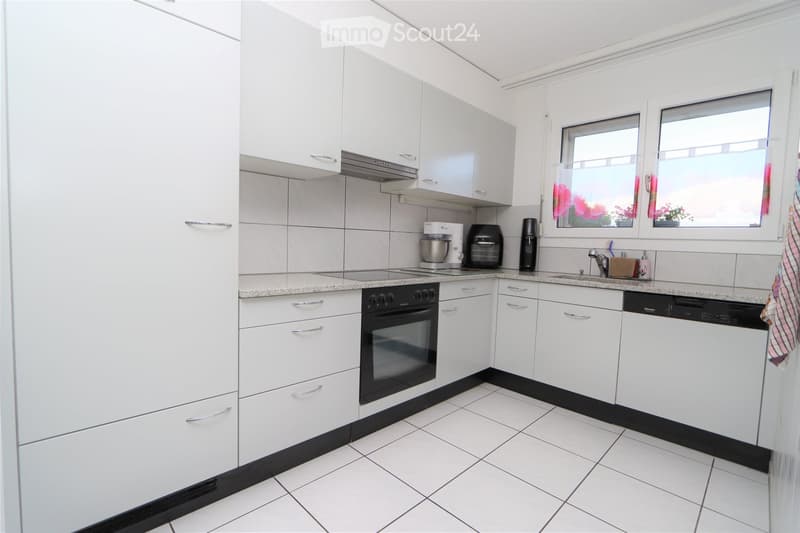 Modern kitchen with white cabinets, tiled walls, and granite countertops. Features an oven, dishwasher, mixer, toaster, and a sink with a faucet.