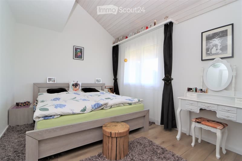 Cozy bedroom with a wooden bed, floral duvet, nightstand, vanity with mirror, and wooden stool.