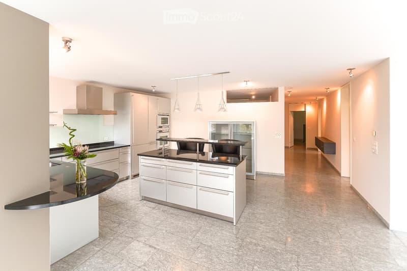Modern kitchen with white cabinets, black countertops, and stainless steel appliances. Features a central island with seating, pendant lights, and a vase with flowers on the counter.