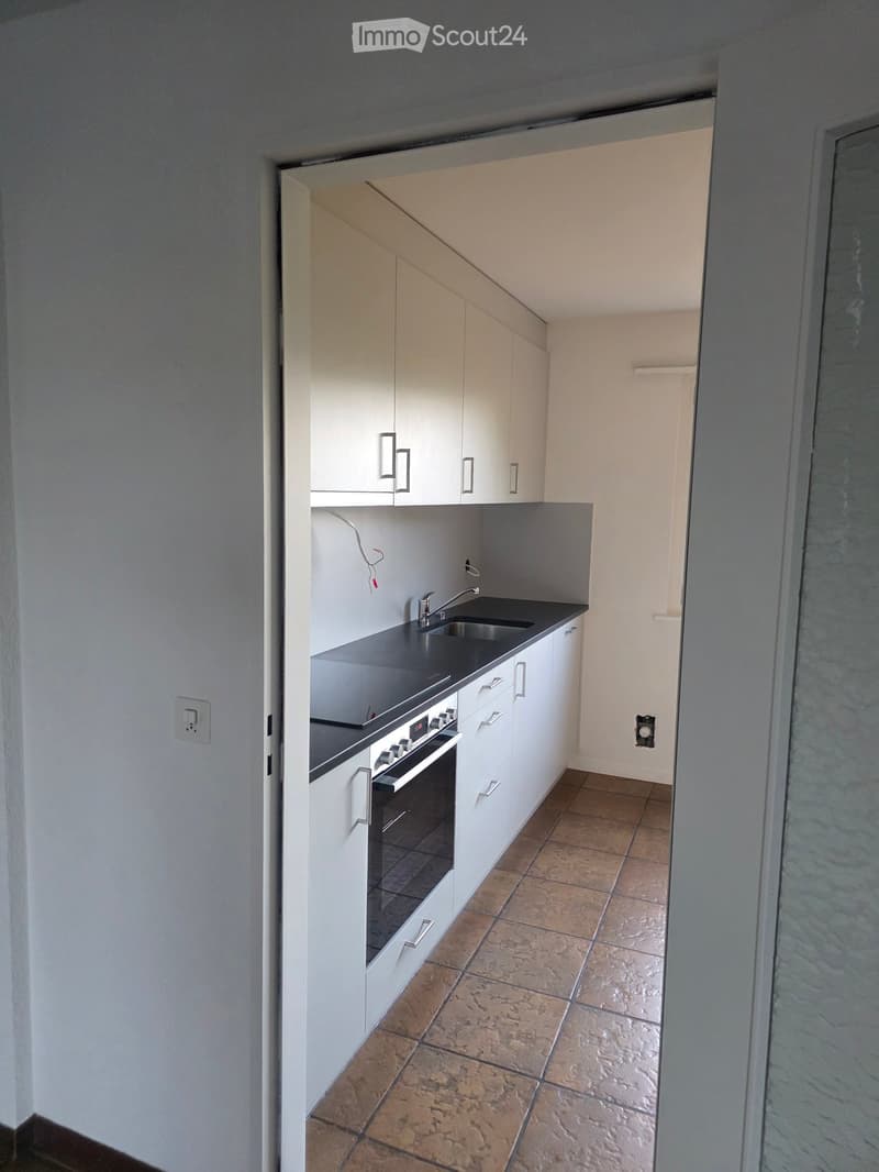 Modern kitchen with white cabinets, black countertop, sink, and built-in oven. Brown tiled floor.