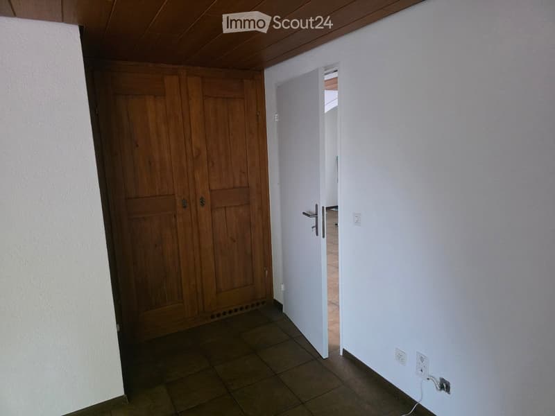 Empty hallway with wooden door on left, white door leading to another room on right, tiled floor, white walls, and visible electrical outlets.