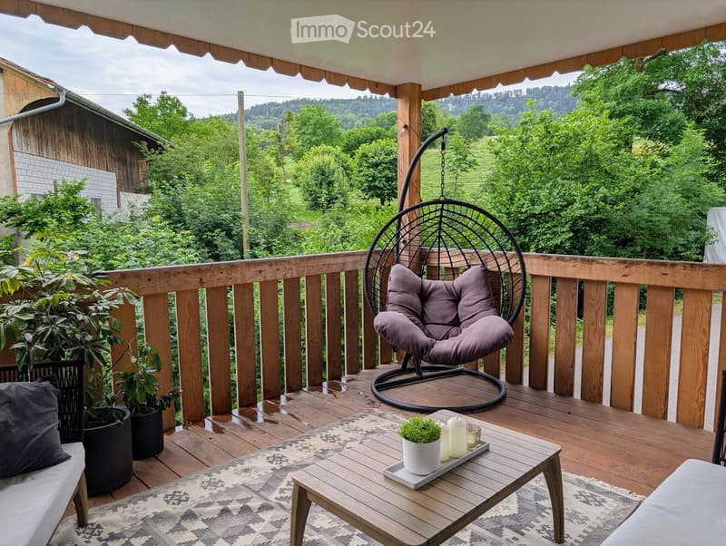 Balcony with wooden decking, hanging wicker chair, coffee table, potted plants, and scenic view of greenery.