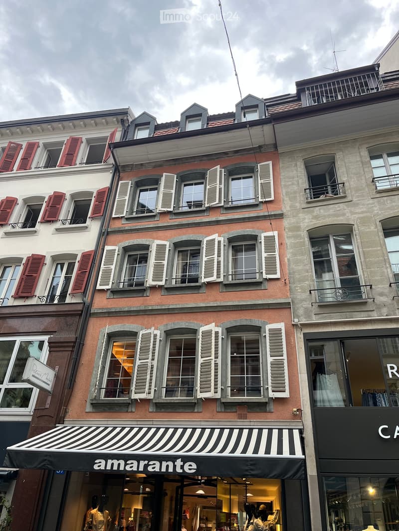 A multi-story building with a pink facade, white shutters, and a striped awning over the storefront labeled "amarante".