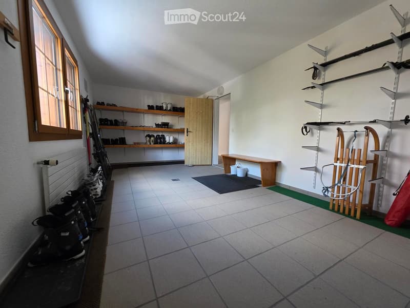 Storage room with wooden shelves, ski equipment, wooden bench, buckets, ski poles on wall, tiled floor, window, radiator