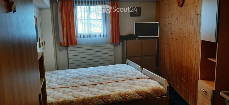 Bedroom with bed, wooden wall, window with curtains, radiator, TV, cabinet, picture frame