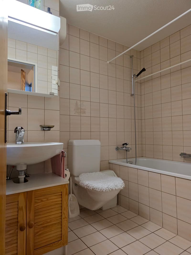 Bathroom with white tiles, white sink, white toilet, bathtub, wooden cabinet, mirror, shower head, and towel rack.