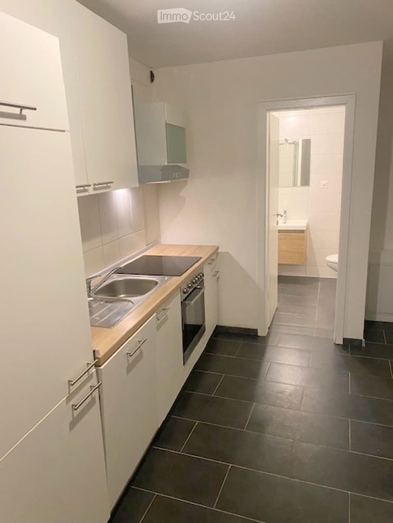 Modern kitchen with white cabinets, stainless steel sink, oven, and a small bathroom visible through an open doorway with a toilet and mirror.
