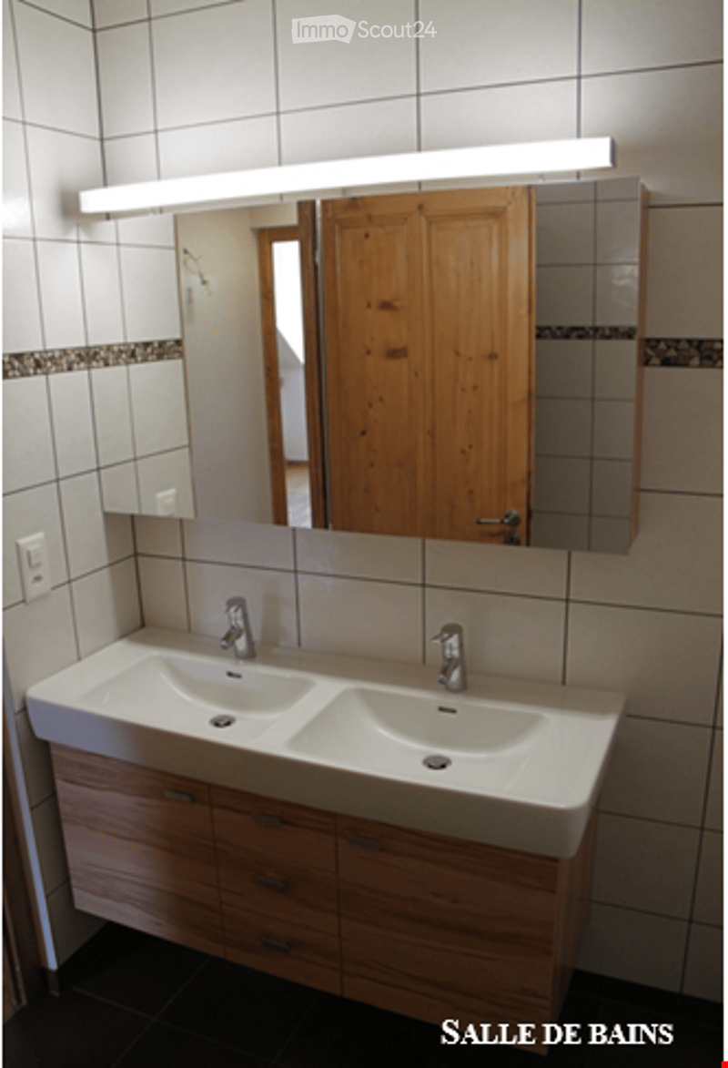 Modern bathroom with double sink, wooden cabinet, large mirror, and sleek lighting fixture above.
