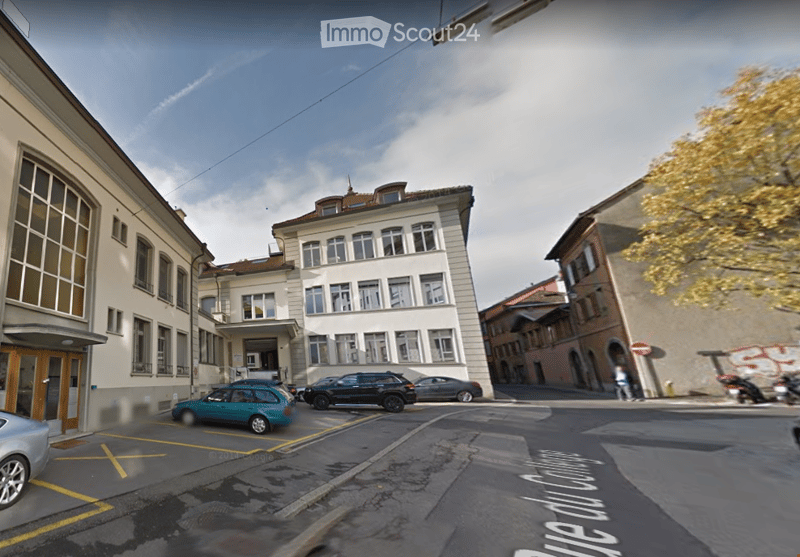 Urban street view with multi-story buildings, parked cars, and a clear sky.