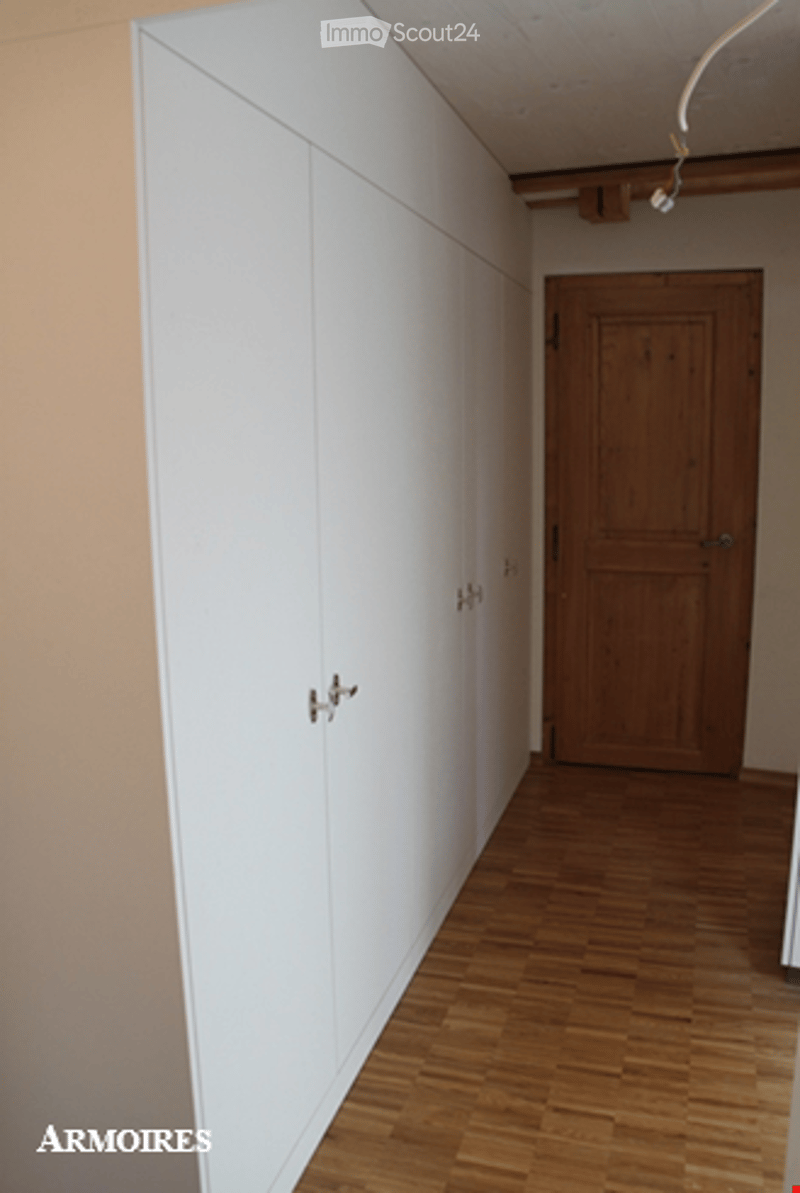 Empty hallway with wooden floor, white built-in closet, and a wooden door at the end.