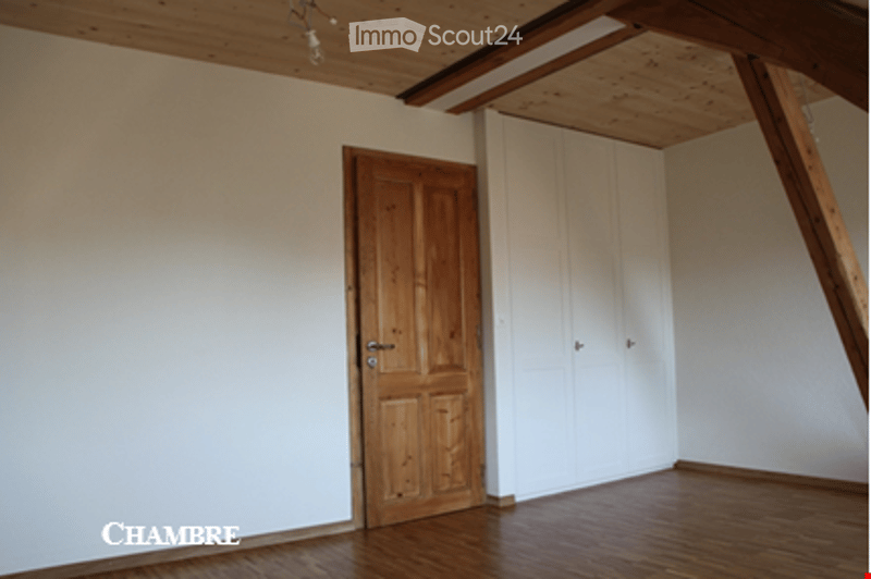 Empty room with wooden floor, white walls, exposed wooden beams on the ceiling, a wooden door, and a white closet.