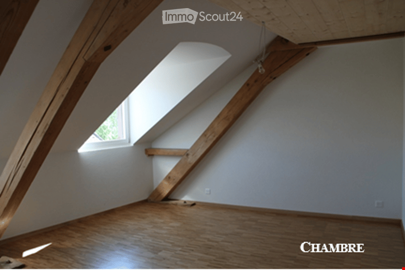 Empty attic room with wooden beams, wooden floor, and skylight window. No furniture or equipment.