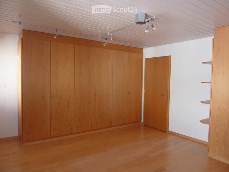 Empty room with wooden floor, white walls, large wooden wardrobe, and a closed door.