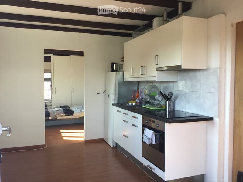 The image shows a modern kitchen with white cabinets, a black countertop, and stainless steel appliances, including a refrigerator, oven, and sink. A dish rack with dishes and utensils is visible on the counter, and a towel hangs from the oven handle. The
