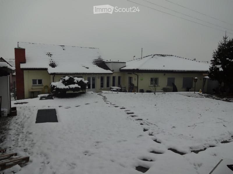 Snow-covered yard in front of a house with a red chimney, surrounded by other houses and trees.