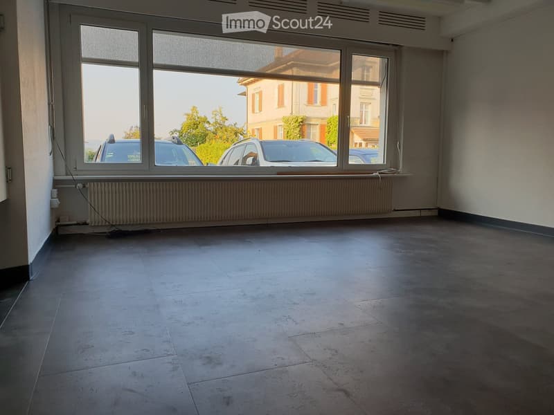 Empty room with large windows, tiled floor, radiator, and visible cars outside.
