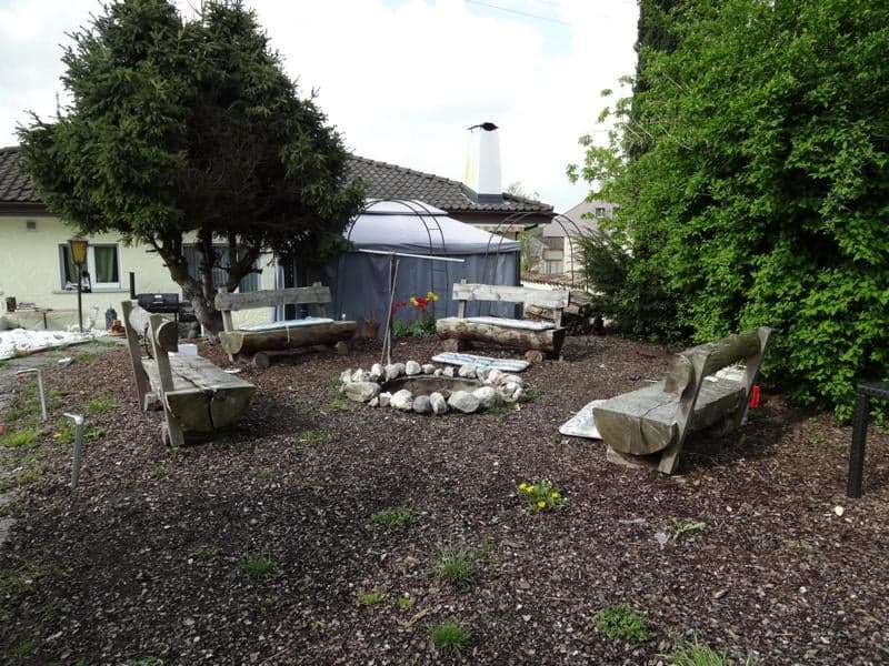 Garden area with stone benches, a fire pit, and surrounding greenery.