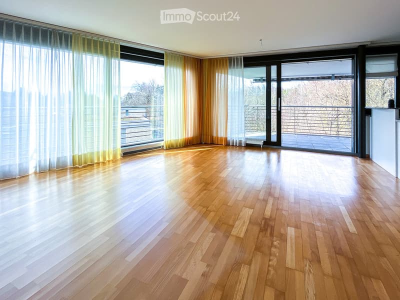 Empty room with wooden flooring, large windows with sheer curtains, and a sliding glass door leading to a balcony.