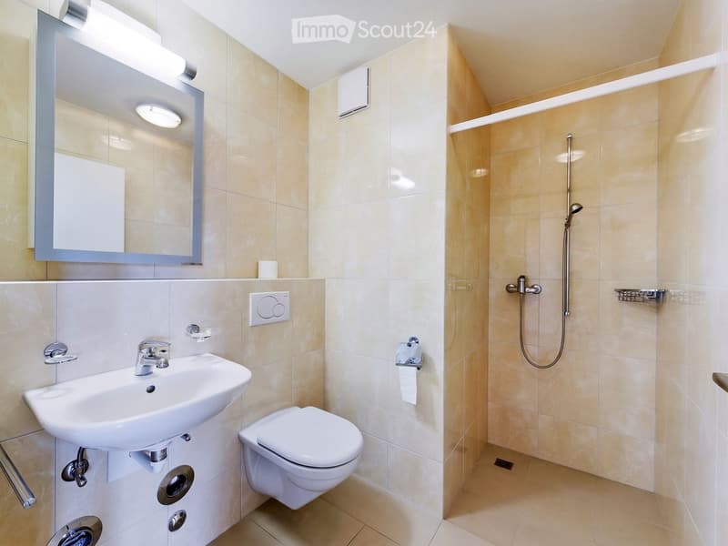 Modern bathroom with beige tiles, a white sink, toilet, mirror, and a shower area with a handheld showerhead.