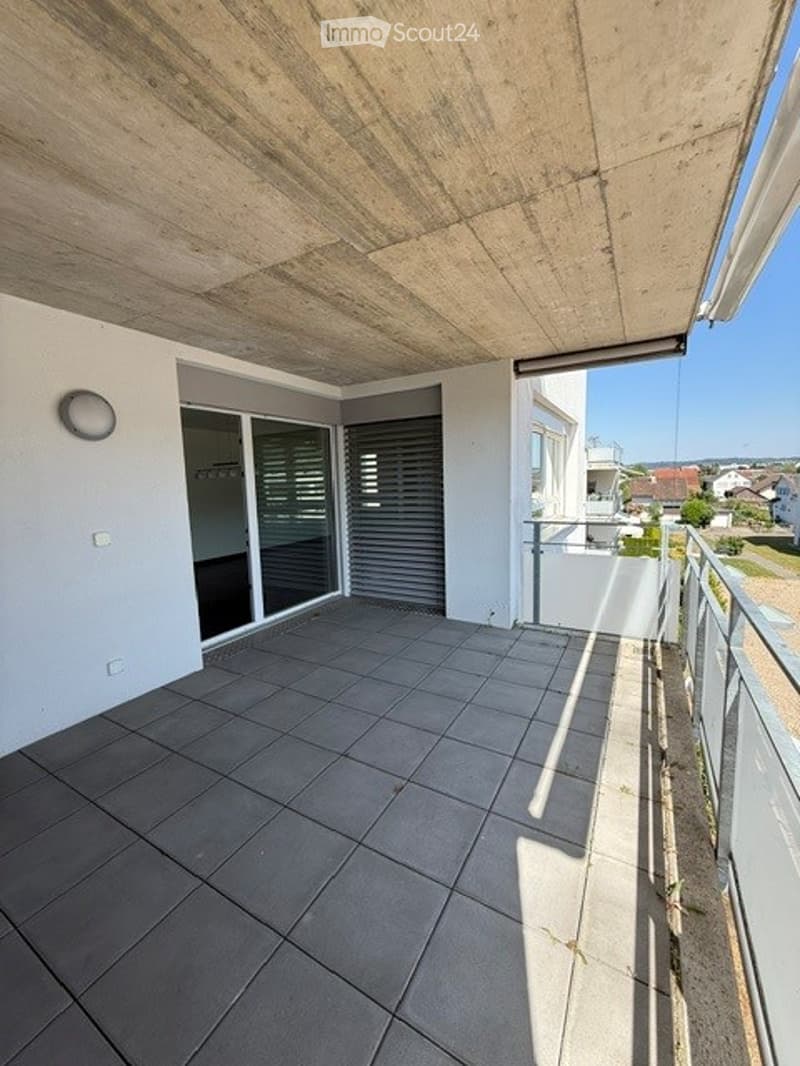 Modern balcony with tiled floor, large sliding glass doors, metal railing, and scenic view of surrounding houses and landscape.