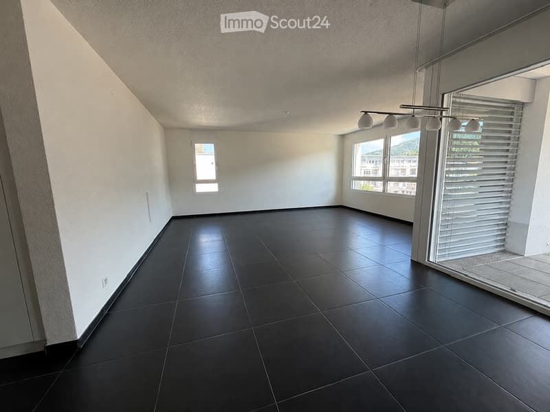 Empty room with dark tiled floor, white walls, large windows with blinds, and a modern light fixture.