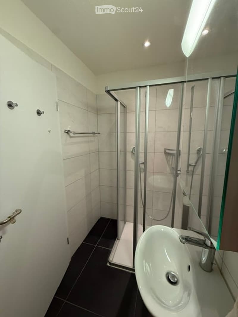 Modern bathroom with white tiles, a glass-enclosed shower stall, a white sink with a chrome faucet, and a towel rack on the wall.