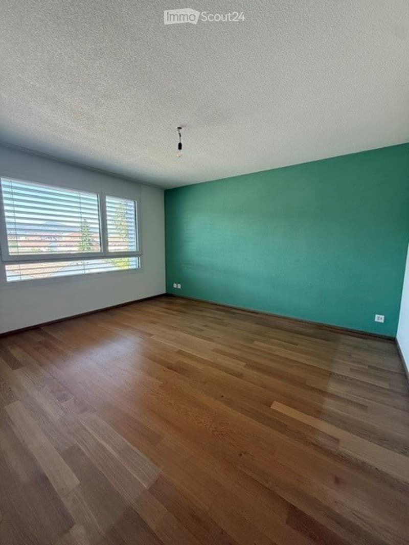 Completely empty room with wooden flooring, white walls, and a large window with blinds. No furniture or equipment present.