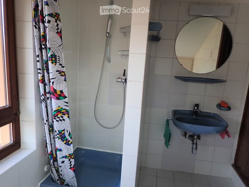 Bathroom with a sink, mirror, shower curtain, and a small window. The shower area has a blue floor and a colorful shower curtain.