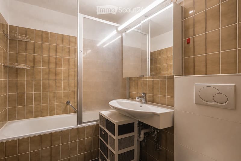 Modern bathroom with beige tiled walls, a white bathtub, a sink with a chrome faucet, a large mirror, and a storage unit beneath the sink.