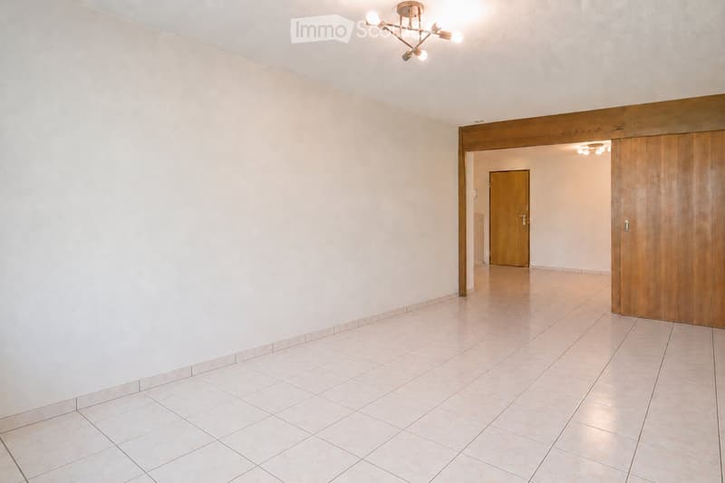 Empty hallway with tiled floor, white walls, wooden doors, and modern lighting fixtures.