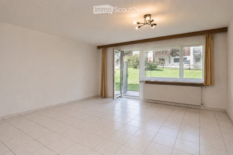 Empty room with tiled floor, large window with curtains, sliding glass door leading to outdoor area, radiator, and ceiling light fixture.