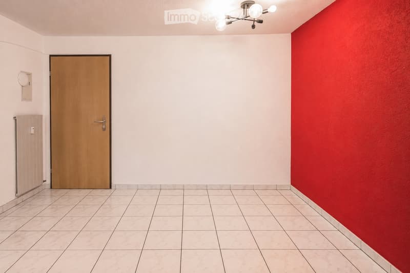 Empty hallway with tiled floor, wooden door, red accent wall, and modern ceiling light fixture.