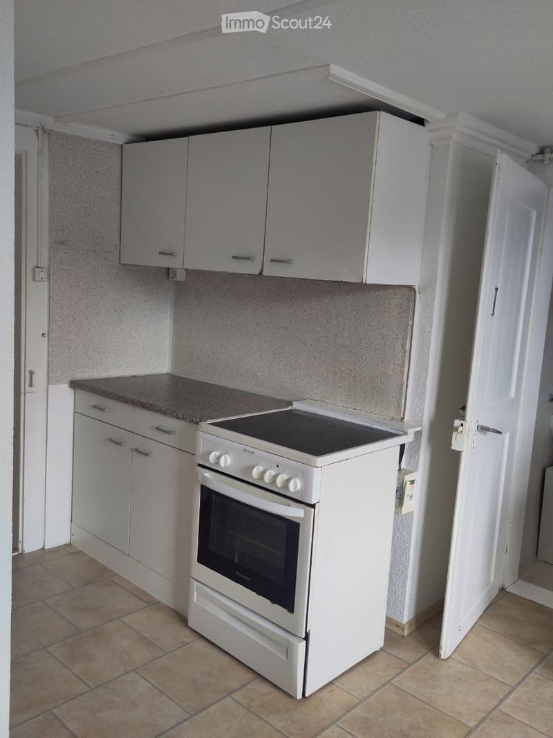 A compact kitchen with white cabinets, a countertop, and a built-in oven. The space features tiled flooring and neutral-colored walls.