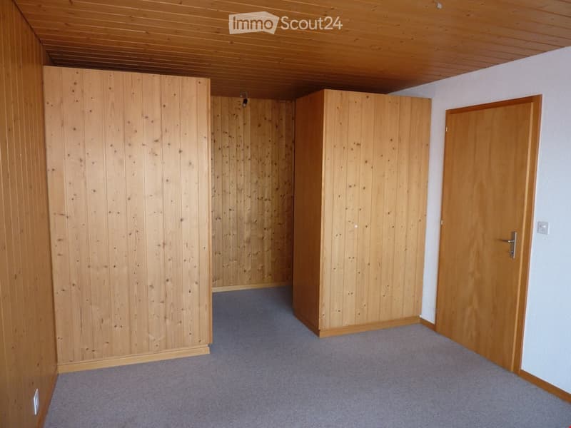 Empty room with wooden walls and cabinets, gray carpet flooring, and a door on the right