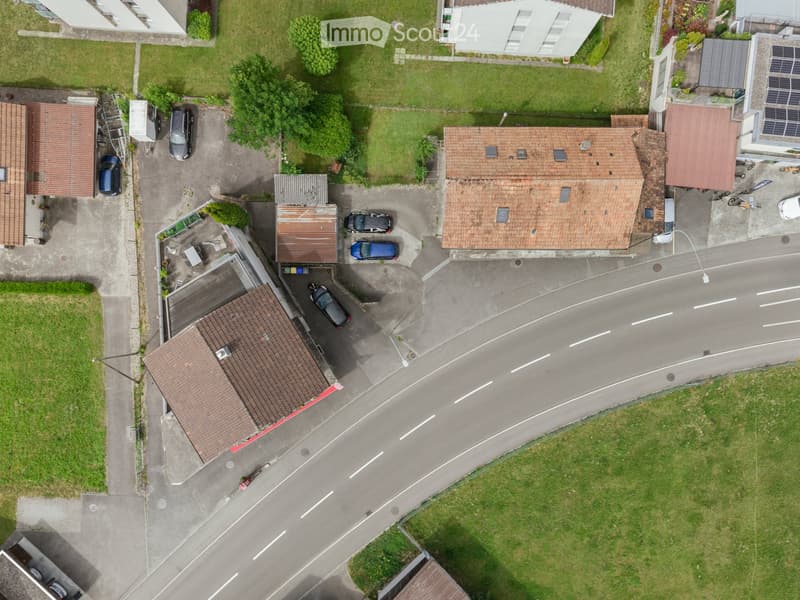 Aerial view of a residential area with multiple houses, parked cars, and surrounding greenery.