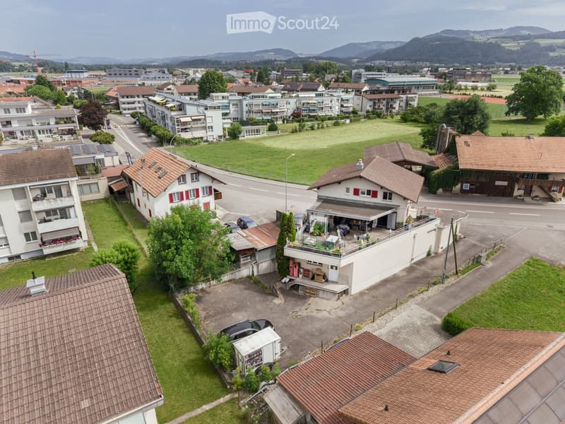 Aerial view of a suburban neighborhood with multiple houses, apartments, and a large green field in the background.