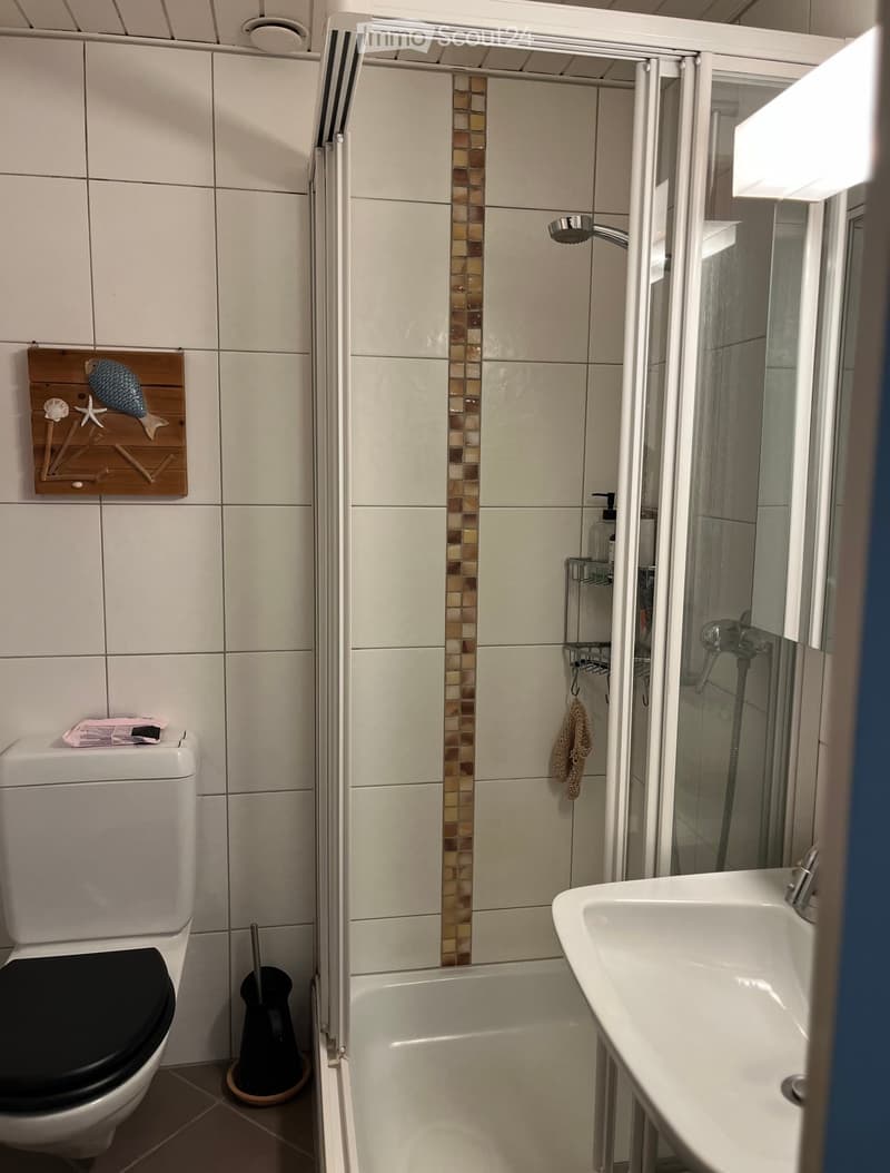 Modern bathroom with white tiles, a bathtub, a toilet, a sink, a shower, and a decorative wall piece featuring a fish and seashells.