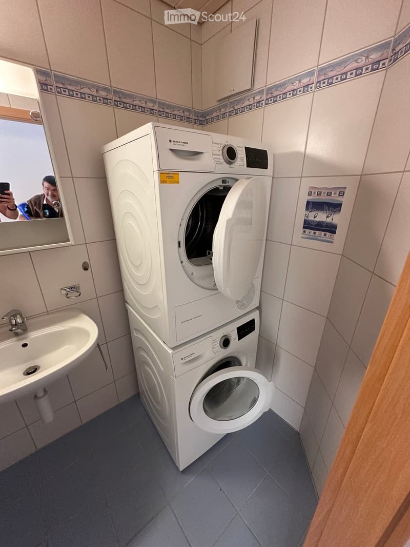Bathroom with a washing machine and dryer unit, a sink, and a mirror.