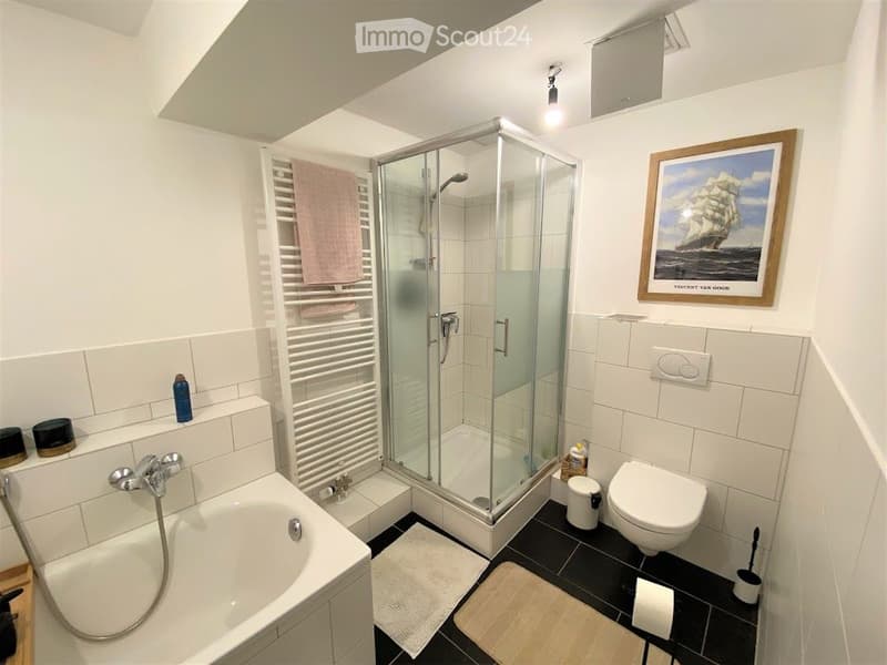 Modern bathroom with a bathtub, toilet, glass-enclosed shower, towel rack, and framed artwork on the wall.