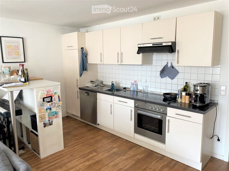 Modern kitchen with white cabinets, stainless steel appliances, wooden flooring, and a small bar area with a piano and stools.