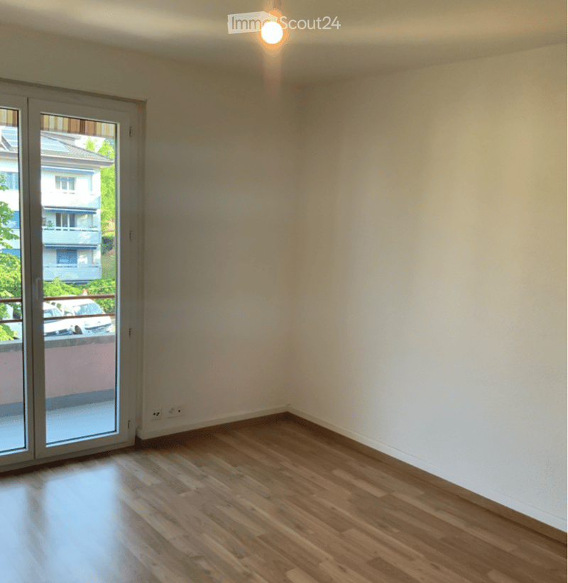 Empty room with wooden flooring, white walls, and a large sliding glass door leading to a balcony.