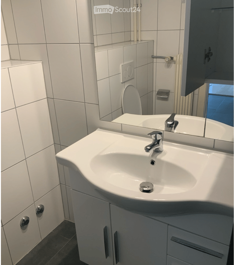 Modern bathroom with a white sink, chrome faucet, mirrored cabinet, and tiled walls.