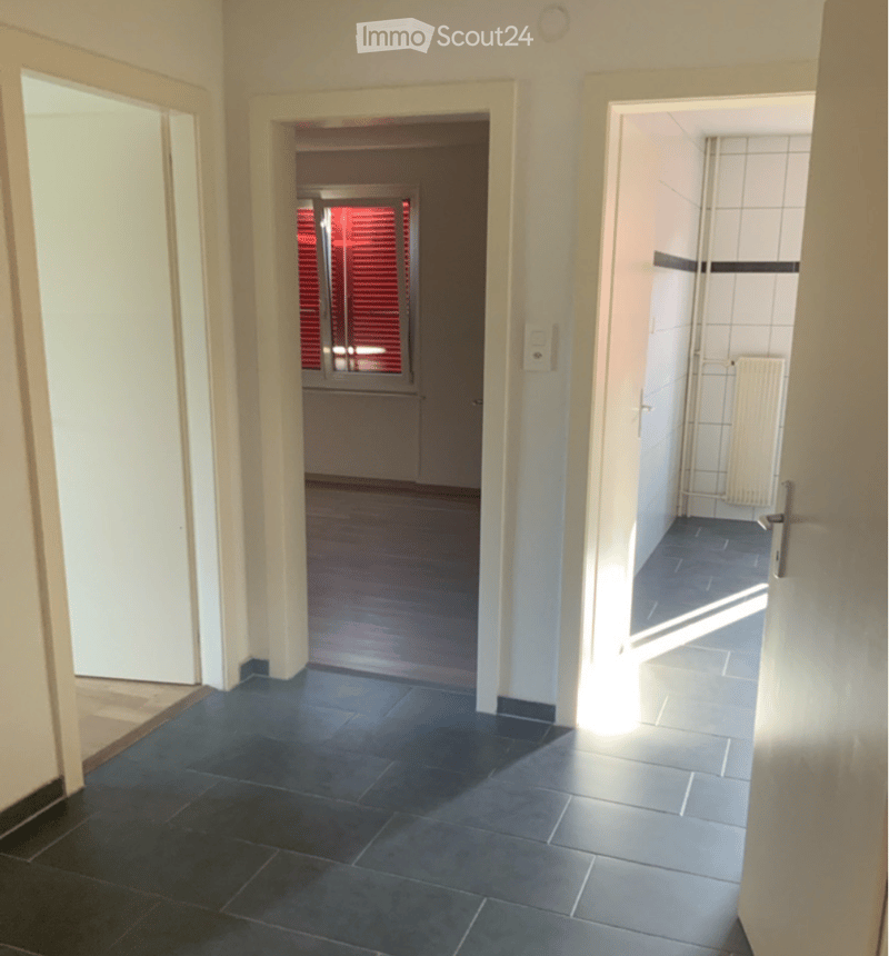 Empty hallway with dark tiled floor, white walls, and multiple doors leading to different rooms.
