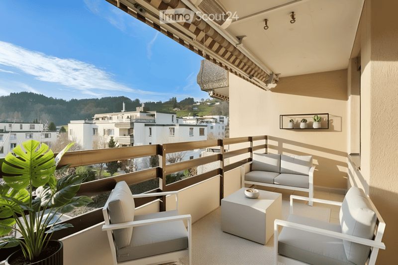 Modern balcony with white furniture, including a sofa, chairs, and a small table, along with a large leafy plant and a small shelf with potted plants.