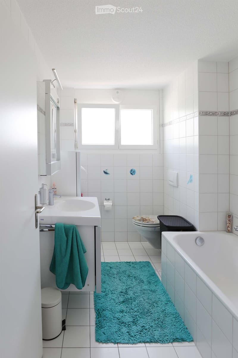Modern bathroom with white tiles, a sink with a mirror, a bathtub, a toilet, and a green bath mat.