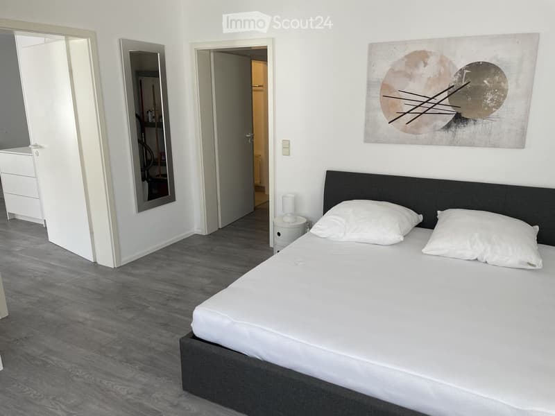 Modern bedroom with a large bed, white bedding, nightstand, mirror, and abstract artwork on the wall.