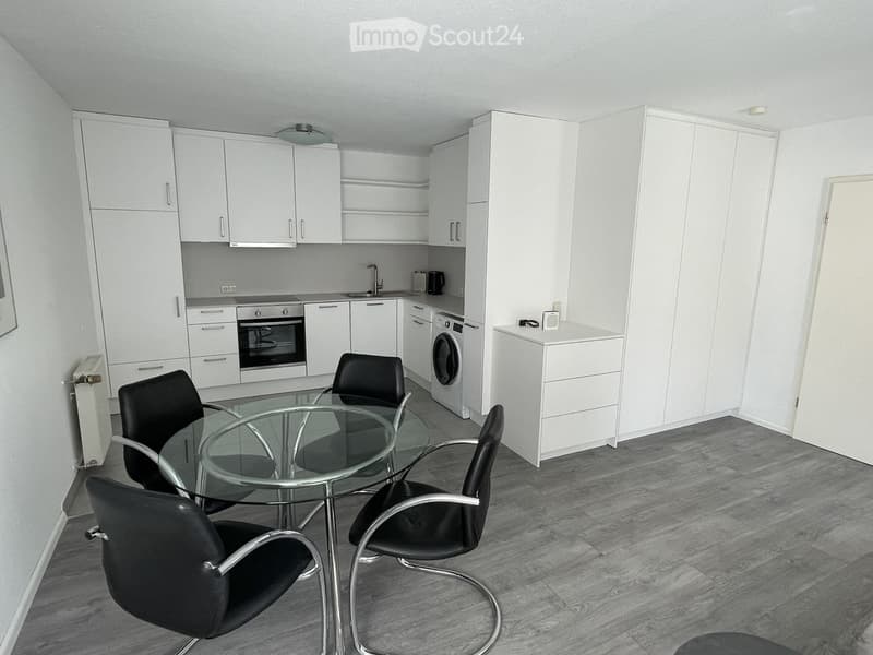 Modern, open-plan kitchen and dining area with white cabinets, a glass dining table with black chairs, and a washing machine.