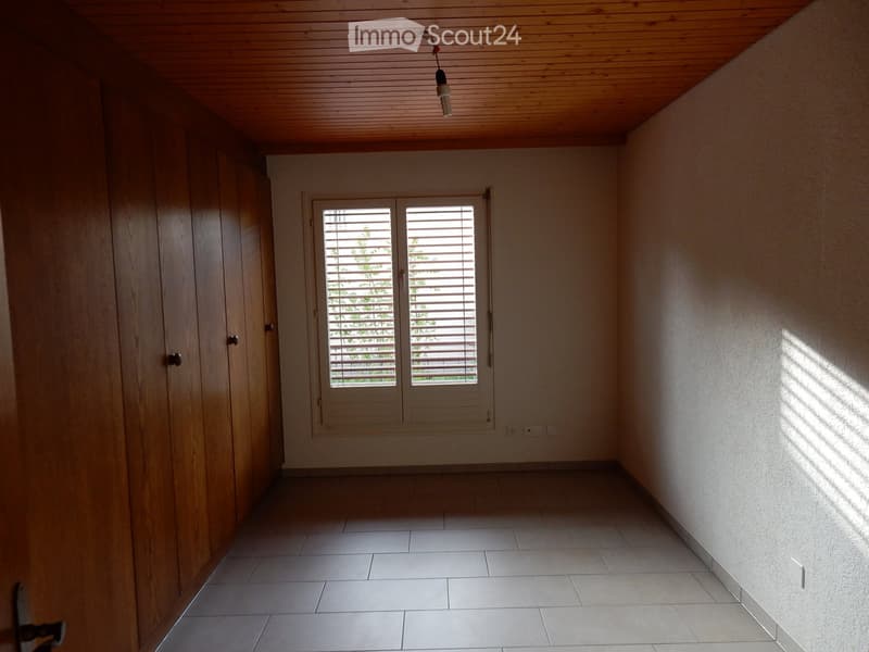 The image shows a room with wooden paneled walls, a tiled floor, and a window with shutters. The room appears to be empty, with no furniture or other objects visible.