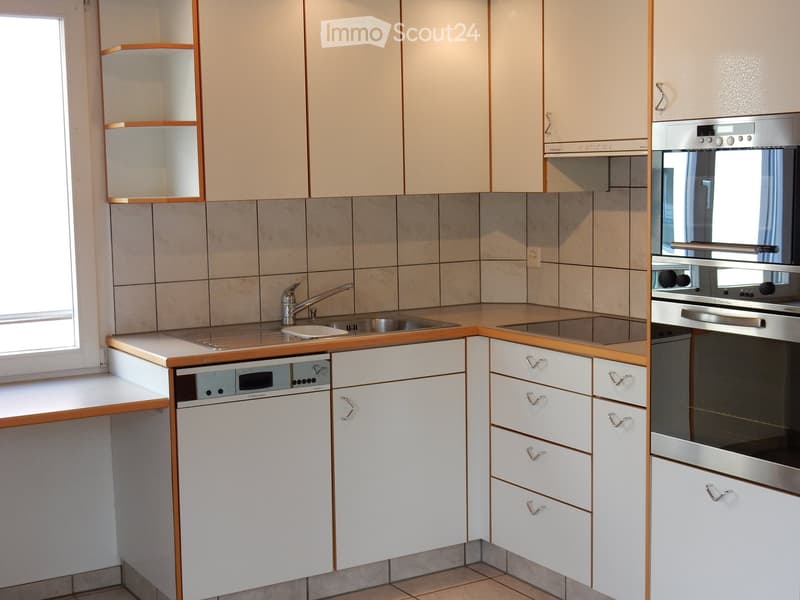 The image shows a modern kitchen with light-colored cabinets, a tiled backsplash, and stainless steel appliances including a dishwasher. The kitchen has an L-shaped layout with a sink and countertop space.